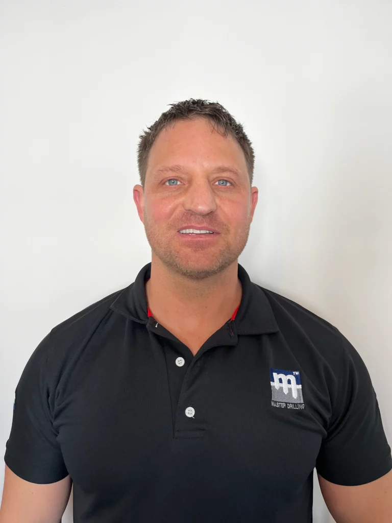 Man wearing a black polo shirt with a logo stands against a plain white background.